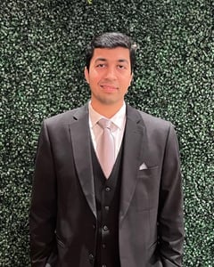 Picture of Kamran Khan Kirmani wearing a suit standing in front of a hedge.
